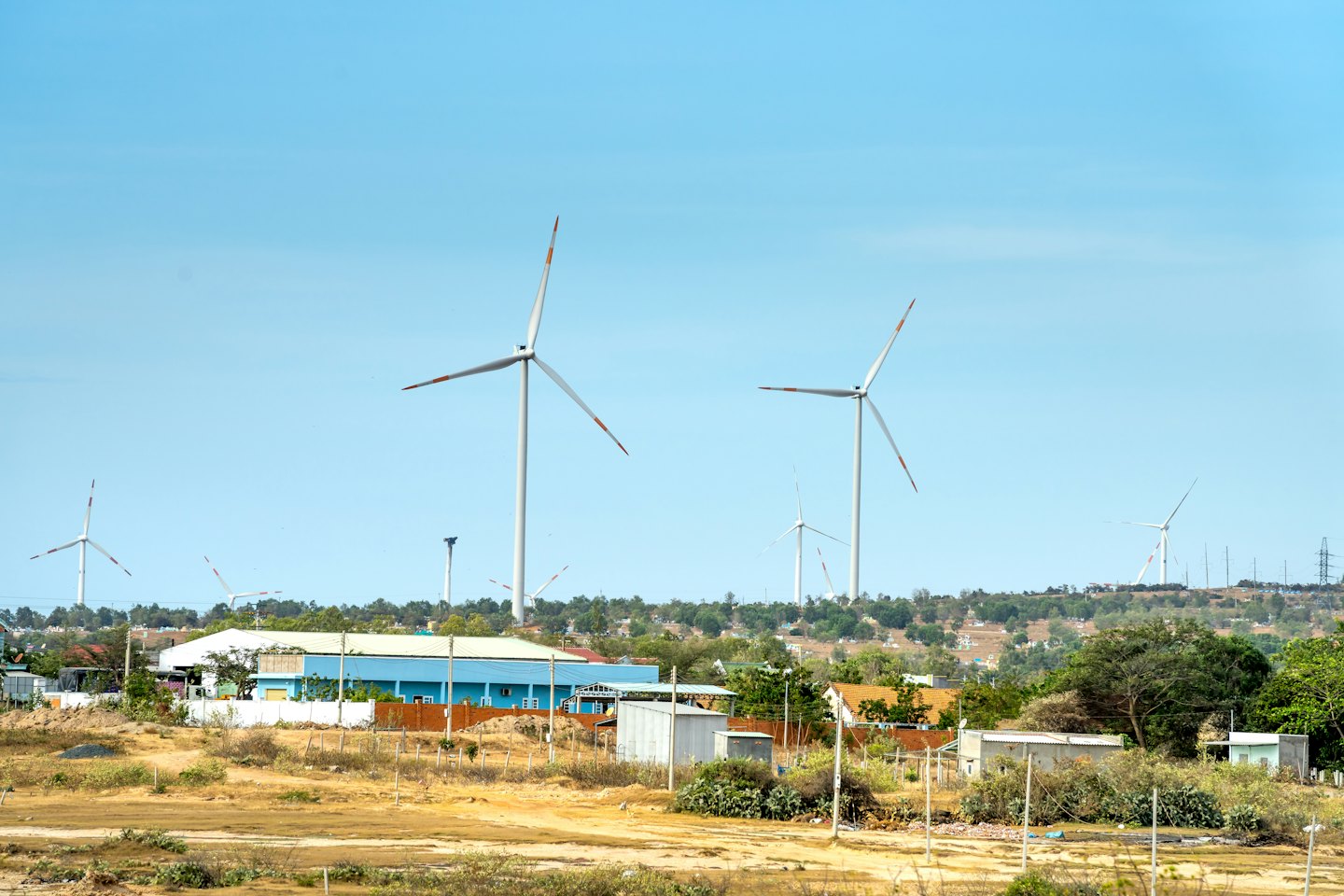 Windkraftanlagen stehen über Gebäuden in ländlicher Landschaft.