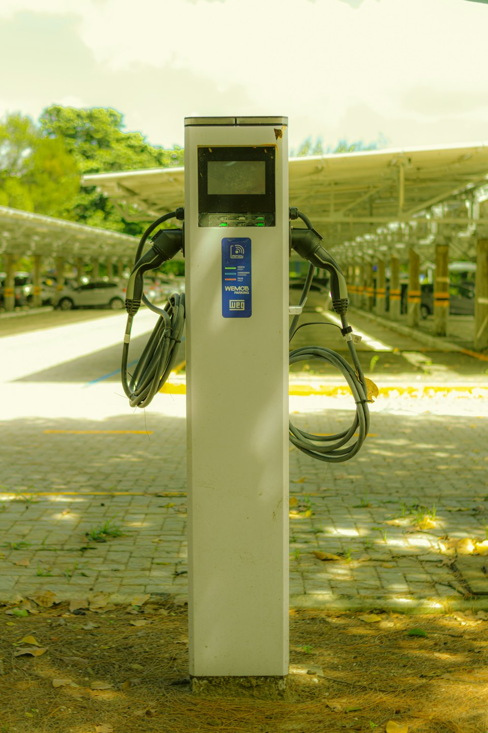 Eine Ladestation für Elektroautos steht auf einem sonnigen Parkplatz.