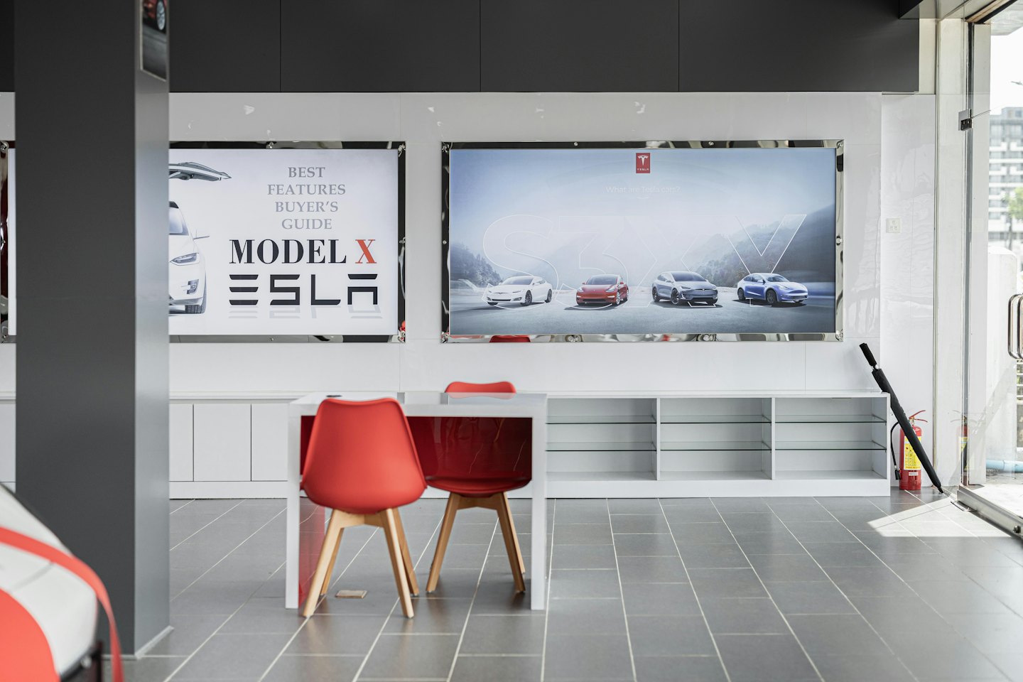 Moderner Ausstellungsraum für Elektroautos mit roten Stühlen und Werbeplakaten.